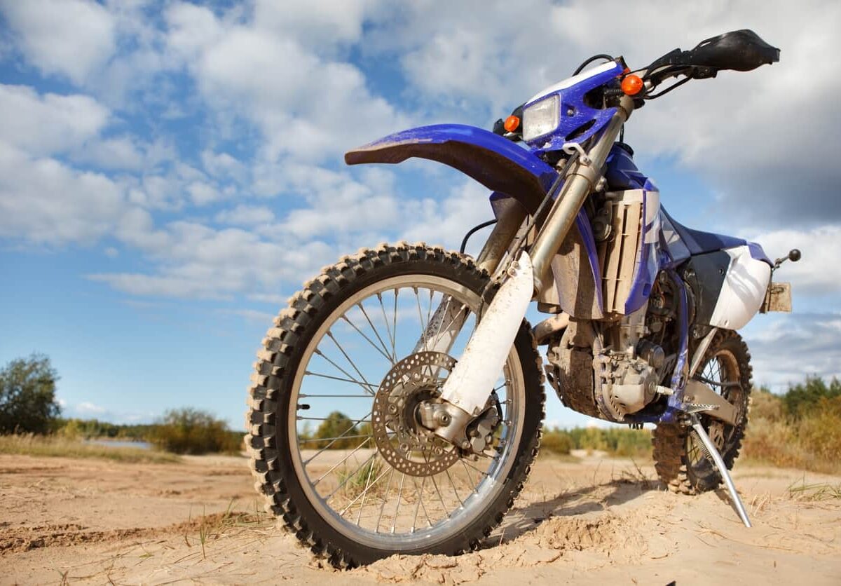 Dirt bike in a dry, flat landscape with shrubs and trees.