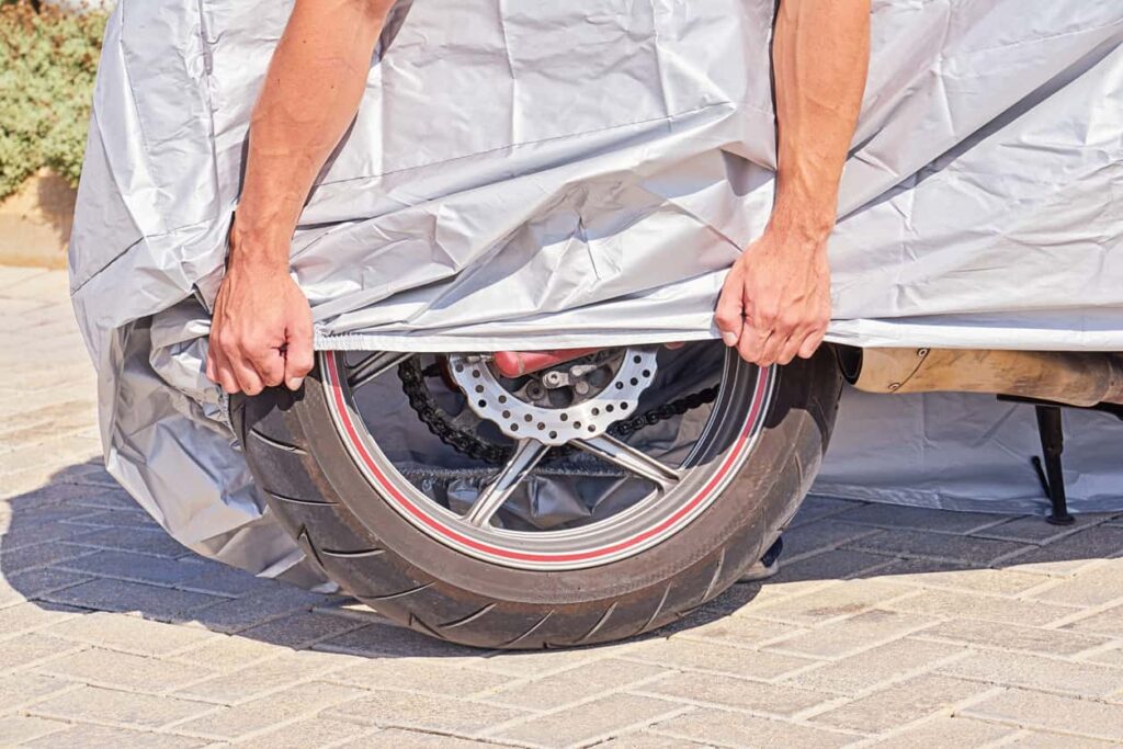 Person pulling a motorcycle tarp down over a tire.