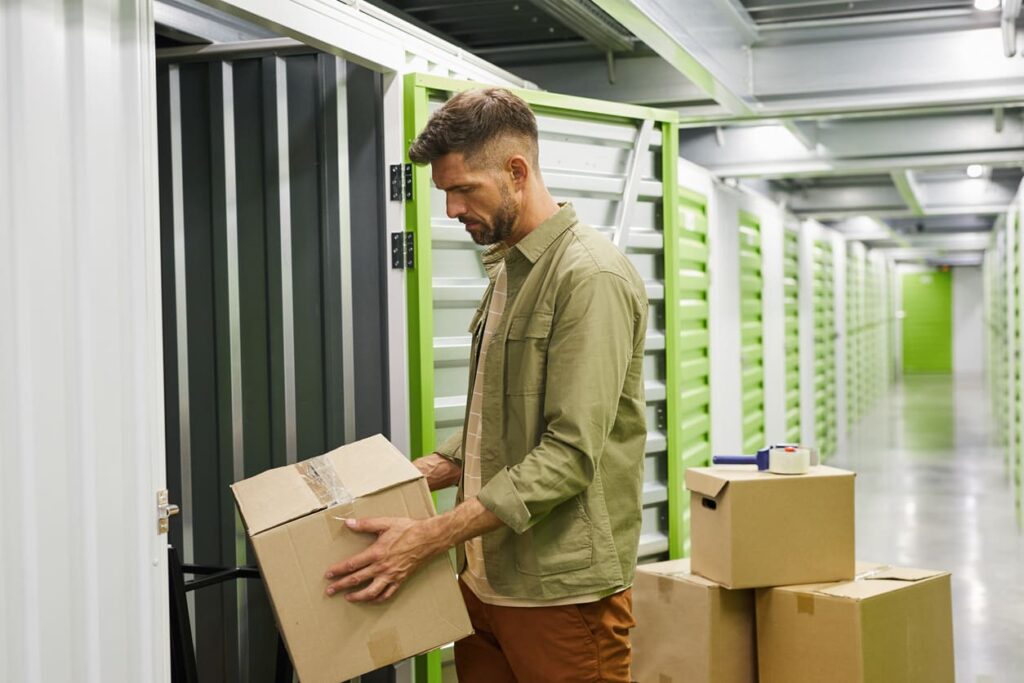 Man moving boxes into a small indoor storage space, potentially a climate-controlled storage unit.