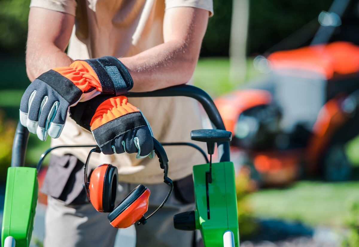 Person with gloves and noise-canceling headphones leaning on a lawn mower.