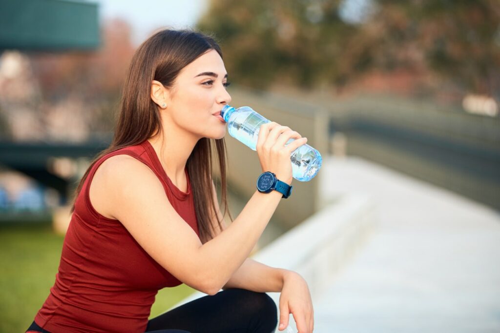 Woman in athletic clothing sitting and sipping a bottle of water