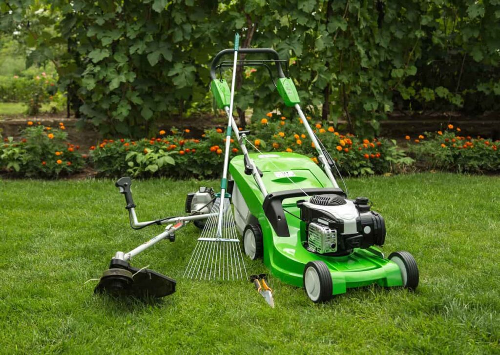 Lawn mower, rake, weedeater, and other lawn equipment grouped in a grassy lawn.