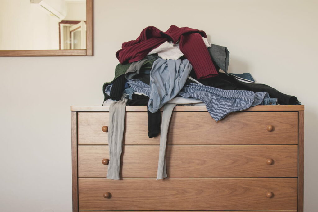 Brown wooden dresser with a messy pile of clothes on top.