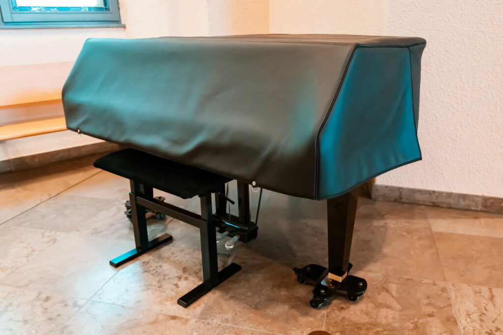 A piano on a brown marble floor with a black leather covering protecting it.