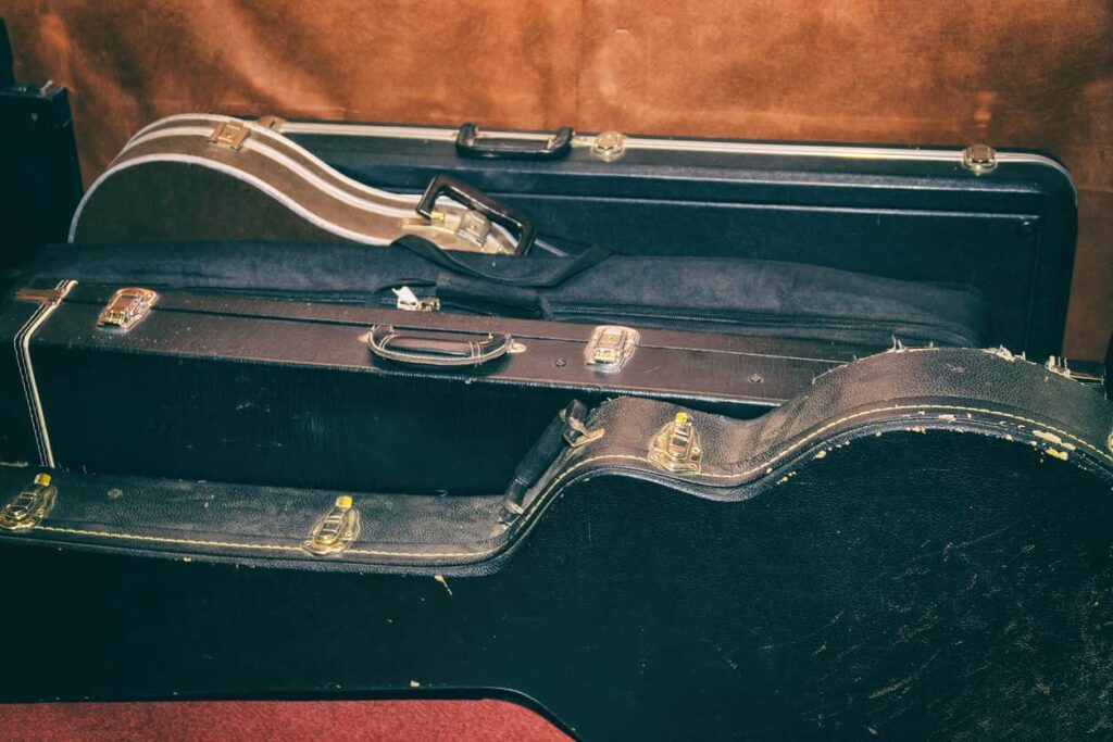 Several musical instruments stored in black leather cases sit on a floor, side by side.
