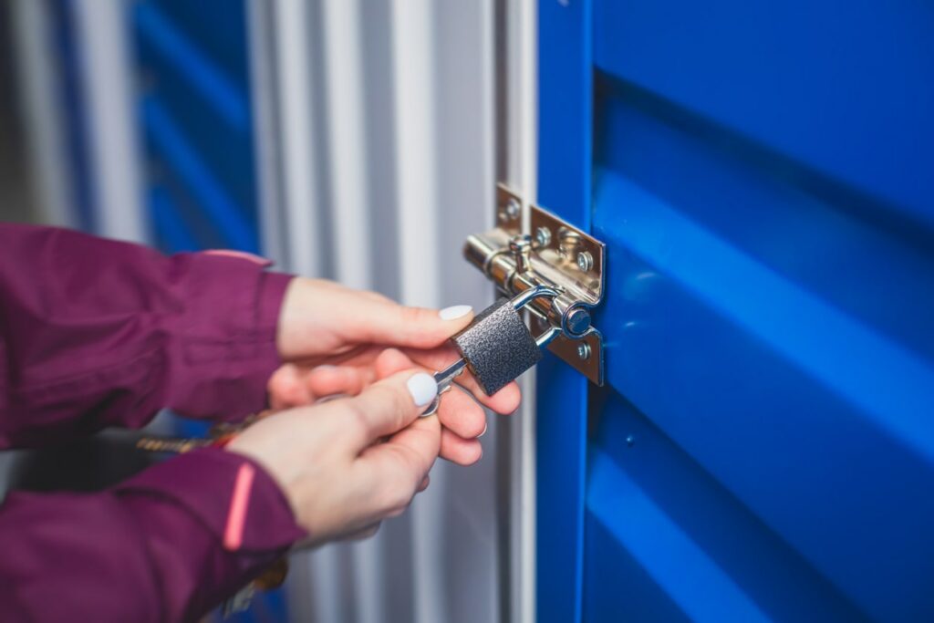 Person wearing a purple jacket turns a key to secure a lock on a storage unit with a blue door.