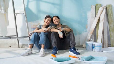 Smiling couple leaning against a partially painted wall.