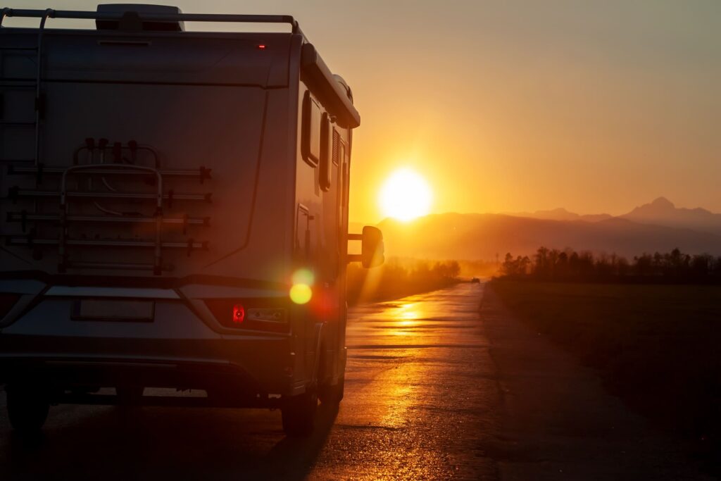 The sun sets on the horizon while an RV drives down the road