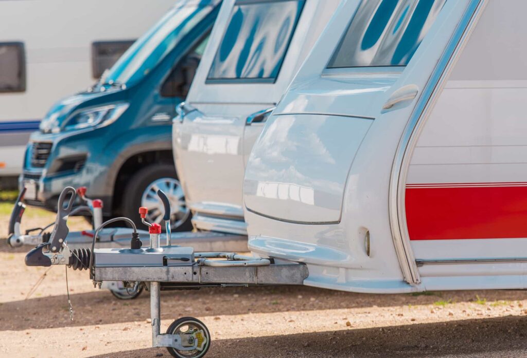 Camper trailers and vans are parked in a row on a gravel lot