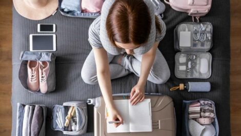 A tourist woman is packing an organized suitcase for vacation and writing a list on paper.