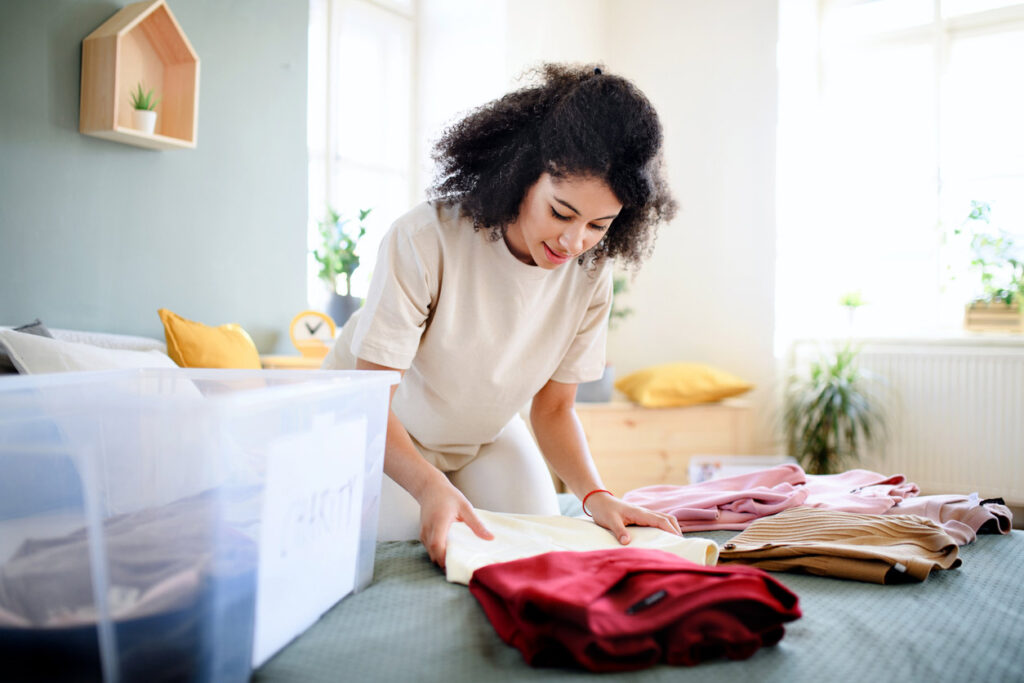 Woman organizing seasonal clothes and setting them on storage bins.